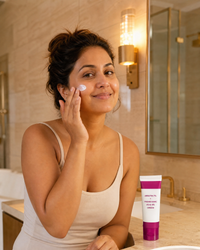 Woman applying Arbutin brightening cream to her cheek in a sunlit bathroom