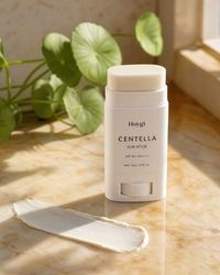 Hoygi Centella sun stick with cap off beside a swipe of cream, centella leaves behind